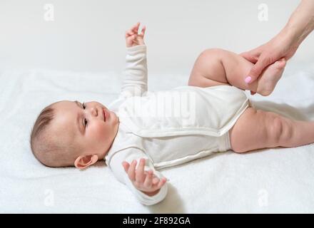 Neugeborenes gesundes Baby, das körperliche Übungen für die Beine und das Hüftgelenk macht. Mit Hilfe der Mutter des Sanitäters. Auf weißem Hintergrund. Stockfoto