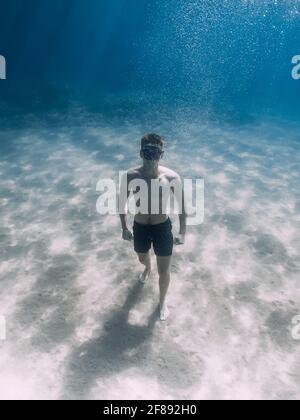 Sportlicher Freitaucher Bleiben Sie auf Sandboden unter Wasser im tropischen Meer. Stockfoto