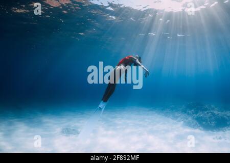 Eine Freitaucherin im Badeanzug mit Flossen gleitet unter Wasser über Sand im tropischen Ozean. Stockfoto