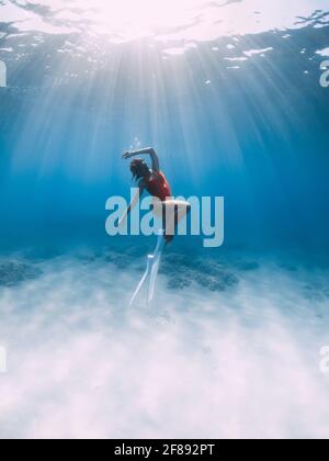 Eine Freitaucherin im Badeanzug mit Flossen gleitet unter Wasser über Sand im tropischen Ozean. Stockfoto