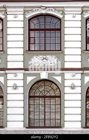 Zwei rechteckige Bogenfenster mit braunem Rahmen an einer grauen Wand. Aus einer Reihe von Fenstern von St. Petersburg. Stockfoto