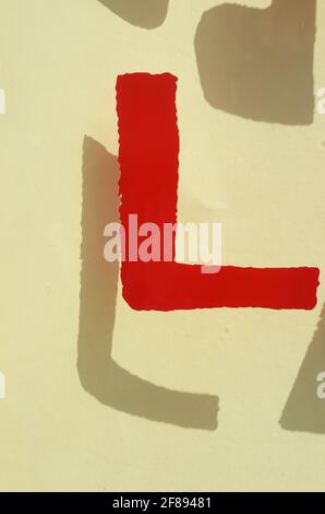 Roter Buchstabe L auf Glas mit Schatten im Hintergrund auf weißer Oberfläche. Stockfoto