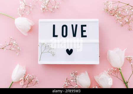 Lightbox mit Text LIEBE und schönen Blumen auf rosa Hintergrund, Draufsicht Stockfoto