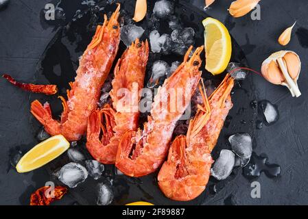 Frische Garnelen mit Zitrone auf dunklem Grund. Rote rohe Garnelen.gefrorene Meeresfrüchte Stockfoto