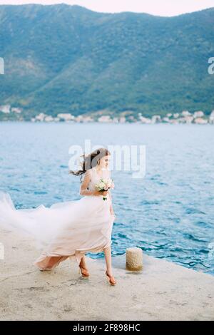 Die Braut hält einen Strauß Rosen in ihren Händen Und spaziert entlang des Piers in der Bucht von Kotor Stockfoto