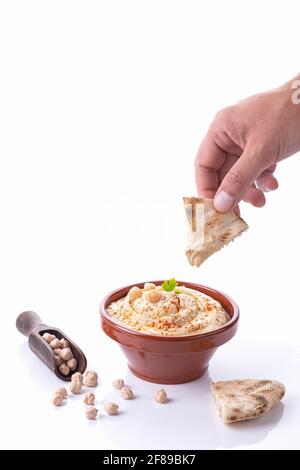 Von Hand eintauchendes Pita-Brot in Hummus isoliert auf weißem Hintergrund mit Kopierraum. Vertikales Format. Stockfoto