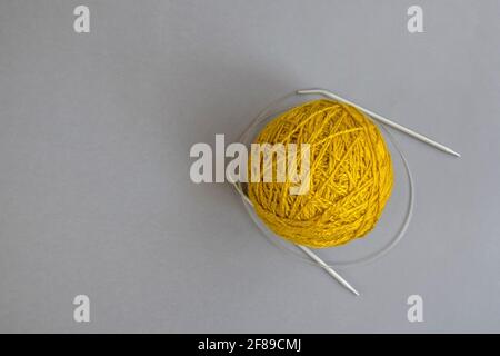 Ein Knäuel aus gelbem Wollgarn und Stricknadeln auf grauem Hintergrund, handgearbeitet, stricken. Nahaufnahme. Speicherplatz kopieren. Selektiver Fokus. Stockfoto