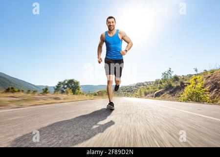 Ganzkörperportrait eines jungen Mannes, der auf einem joggt Asphaltierte Straße zur Kamera Stockfoto