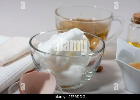 Inhaltsstoffe der Maske „Eierweiß“. Geschlagenes Eiweiß, Mandelöl, Honig, Kamillentee. Hausgemachte Kosmetik. Nahaufnahme. Stockfoto