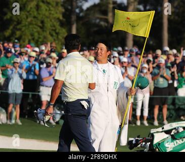 Augusta, USA. April 2021. Nachdem er die Masters mit einem Schlag gewonnen hatte, dankt Hideki Matsuyama seinem Caddie Shota Hayafuji auf dem 18. Green, der sich noch lange Zeit hielt, um den Flaggenstock wieder in den Cup zu stecken und sich einen Moment Zeit zu nehmen, um sich am Sonntag, dem 11. April 2021, in Augusta, Georgia, dem Augusta National Golf Club Course, zu beugen. (Foto von Curtis Compton/Atlanta Journal-Constitution/TNS/Sipa USA) Quelle: SIPA USA/Alamy Live News Stockfoto