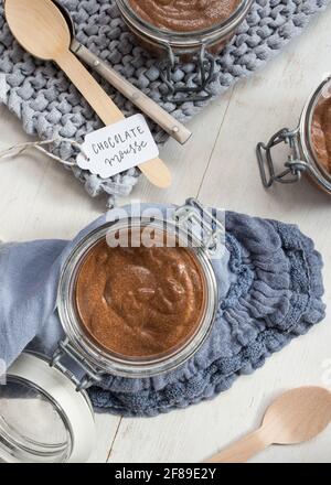 Nahaufnahme eines ungedeckten Glases mit Schokoladenmousse auf einer eleganten blauen Serviette, umgeben von ein paar Löffeln. Stockfoto