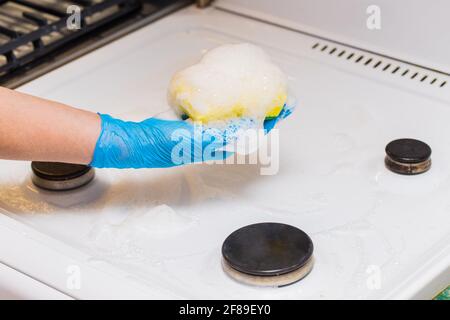 Frauenhand in einem Haushaltshandschuh Waschschwamm mit Schaum ein schmutziger Gasherd und Brenner in der Küche, Nahaufnahme. Stockfoto