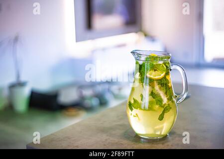 Eiskalte Limonade mit Minze und Zitrone. Der Krug steht auf der Küchentheke. Hintergrund ist unscharf. Stockfoto