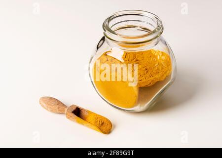 Gewürzpulver in Glas und Holzlöffel auf weißem Hintergrund. Stockfoto