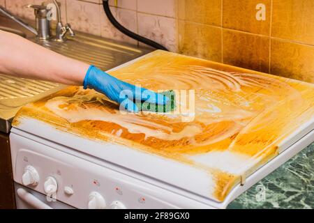 Frau Hausfrau Hand in einem Haushalt Handschuh wäscht eine schmutzige Beschichtung auf einem Gasherd auf Küche Hintergrund, Nahaufnahme. Stockfoto