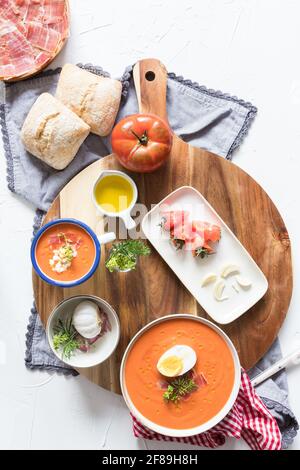 Gesunde Zutaten für eine spanische Tomatensuppe, ein Salmorejo, auf einem hölzernen Schneidebrett auf weißem Hintergrund. Stockfoto