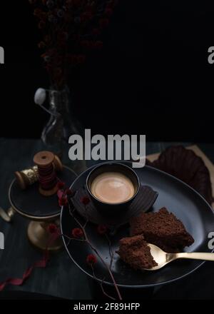 Nahaufnahme eines eleganten Tabletts mit einem schäumenden Kaffee, einer Scheibe Kuchen und einem goldenen Löffel darüber mit einem kleinen Stück Kuchen. Stockfoto