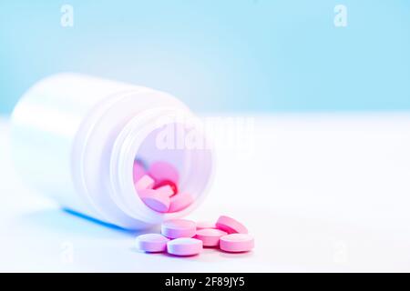 Rosa Pillen werden aus einer Plastikflasche Medizin auf einen weißen Tisch gegossen. Pharmaindustrie. Gesundheitswesen und Medizin. Pharmakonzept. Stockfoto