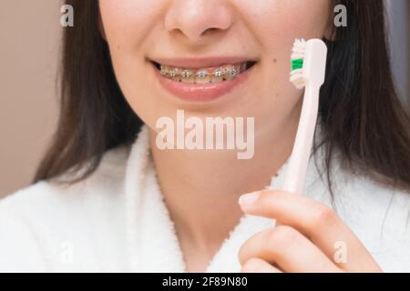 Eine Frau mit Zahnspange oder Halterung putzt sich ihre Zähne mit einer rosa Zahnbürste im Badezimmer. Zahnpflege. Ausrichten und Richten der Zähne. Stockfoto