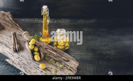 Grüne Oliven in einem Glasgefäß auf einem Holzhintergrund, eine Flasche Olivenöl auf einem alten Holzhintergrund. Nahaufnahme, Kopierbereich. Stockfoto