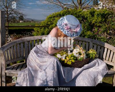 Junge Frau in einer Osterhaube und in der Schulter Langer Dreass, der auf der Bank auf der Aussichtsplattform sitzt Und sich über den Blumenkorb lehnend Stockfoto