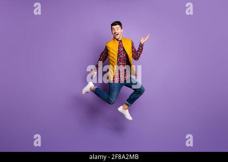 In voller Größe Profilfoto des optimistischen Kerl laufen Sprung tragen hemd Jeans Weste isoliert auf violettem Hintergrund Stockfoto