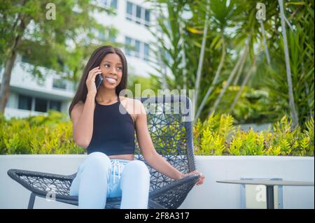 Porträt einer jungen afroamerikanischen Frau lässig sitzen und Mit dem Smartphone im Freien Stockfoto