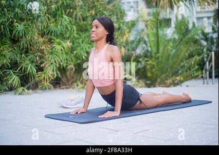 Porträt einer jungen afroamerikanischen Frau, die sich im Yoga dehnt Stellen Sie sich tagsüber draußen vor tropisch grünem Hintergrund auf Stockfoto