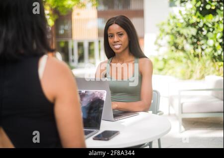 Porträt einer jungen afroamerikanischen Frau, die mit einem Laptop arbeitet Computer und Gespräche mit Kollegen außerhalb Stockfoto