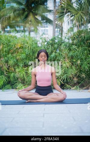 Porträt einer jungen afroamerikanischen Frau, die sich im Yoga dehnt Stellen Sie sich tagsüber draußen vor tropisch grünem Hintergrund auf Stockfoto