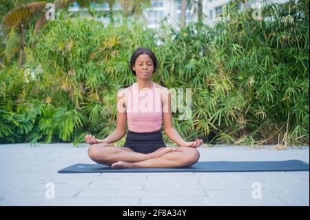 Porträt einer jungen afroamerikanischen Frau, die sich im Yoga dehnt Stellen Sie sich tagsüber draußen vor tropisch grünem Hintergrund auf Stockfoto