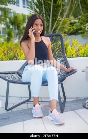 Porträt einer jungen afroamerikanischen Frau lässig sitzen und Draußen telefonieren Stockfoto