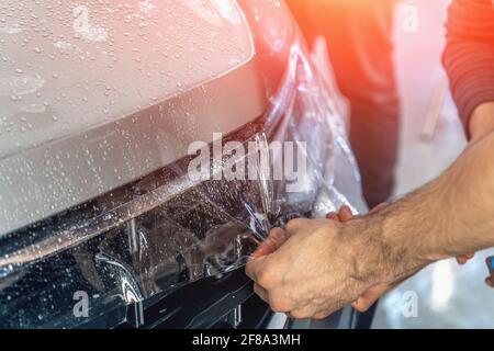 Autoschutzfolie oder PPF-Verfahren zum Einwickeln und Installieren auf der Motorhaube durch Detailarbeiter Hände, Nahaufnahme. Stockfoto