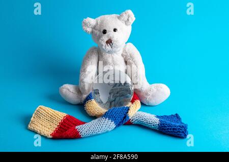 Hintergrund des Autismus-Bewusstseins. Teddybär sitzt umarmende Glaskugel mit gestricktem Schal auf blauem Hintergrund gewickelt. Speicherplatz kopieren. Stockfoto