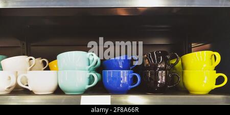 Große Auswahl an bunten niedlichen Kaffeetassen in einem angeordnet Linie auf einem silbernen Küchentisch Stockfoto