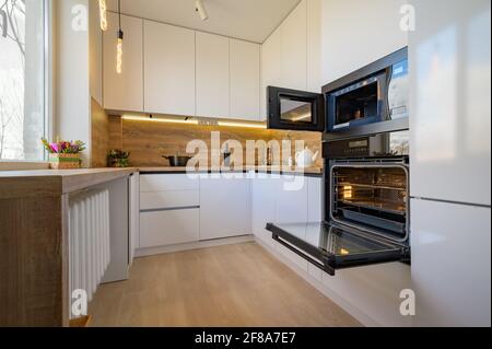 Moderne weiße und beige Holzküche mit Backofen geöffnet Stockfoto