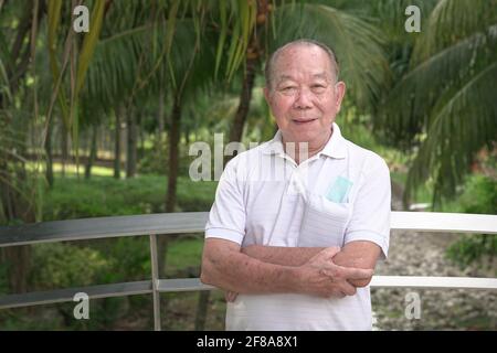 Porträt eines älteren asiatischen Mannes, gekreuzte Hände. Im Park. Stockfoto