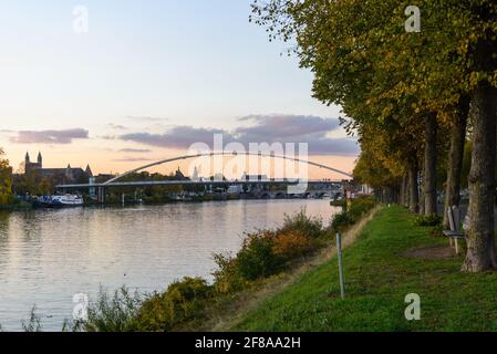 Flussufer des Maas und Hoge Brug, moderne Fußgängerbrücke, während der Sonnenuntergangszeit und dramatischer Dämmerungshimmel in Maastricht, Niederlande Stockfoto