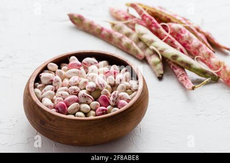 Bunte rosa und weiß geschälte Cranberry Borlotti Bohnen in Holz Schüssel mit Muschelbohnen im Hintergrund Stockfoto