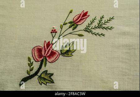 Ein schöner bestickter Zweig mit kleinen Rosen und einer Knospe, einem Nadelzweig und kleinen roten Beeren auf einem weißen Baumwollstoff. Stockfoto