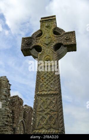 Moosig grüner Stein Keltisches Kreuz mit geschnitztem Stein Herz mit Steinruinen gegen den wolkigen blauen Himmel in Irland Stockfoto