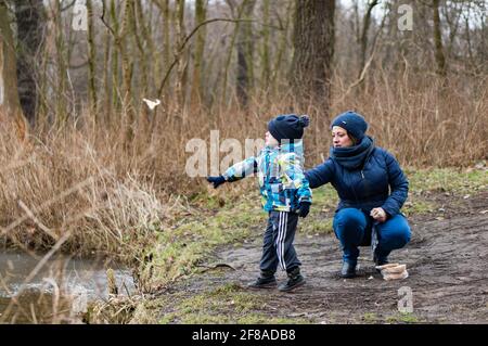 POZNAN, POLEN - 18. Feb 2018: Nicht identifizierter Kleinkind Junge und Frau werfen Brot in einem Teich am Debinski Wald an einem kalten Wintertag Stockfoto