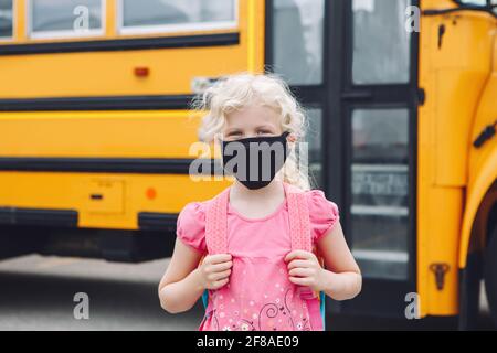 Happy girl Student in Stoff Gesichtsmaske von gelben Schulbus im Freien. Kind mit persönlicher Schutzausrüstung im Gesicht. Bildung und zurück zur Schule Stockfoto