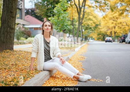 Schöne kaukasische Frau mittleren Alters mit kurzen Haaren sitzt im Herbst Straße im Freien. Frau mit kurzem Haarschnitt in legerer Kleidung im Park. Stockfoto