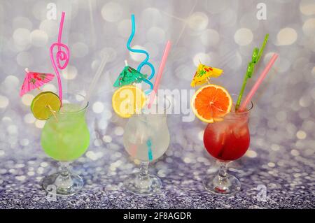 Drei große Gläser mit Zitrusfrüchten, Eis, Trinkhalmen und Cocktailschirmen, dekoriert mit Scheiben aus Limette, Zitrone und Grapefruit auf grauem Hintergrund. C Stockfoto