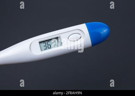 Hand hält weißes elektronisches Thermometer im Hintergrund mit Packungen von Tabletten und blauer medizinischer Gesichtsmaske. Stockfoto