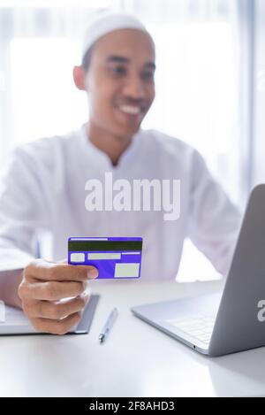 muslimischer asiatischer Mann mit Kreditkarte für Online-Shop-Zahlung Stockfoto