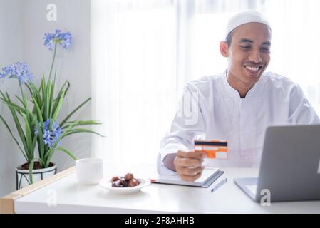 muslimischer asiatischer Mann mit Kreditkarte für Online-Shop-Zahlung Stockfoto