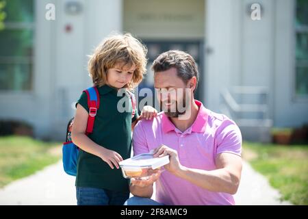 Schuljunge, der mit Vater zur Schule geht. Schuljunge und Eltern im Hemd mit Lunchbox. Schulessen für Kinder. Stockfoto