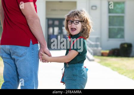 Vater geht Sohn zur Schule. Elternteil und Schüler des Grundschuljungen mit Rucksack. Porträt eines staunenden Nerd-Schuljungen, der Lehrer in der Hand hält. Stockfoto